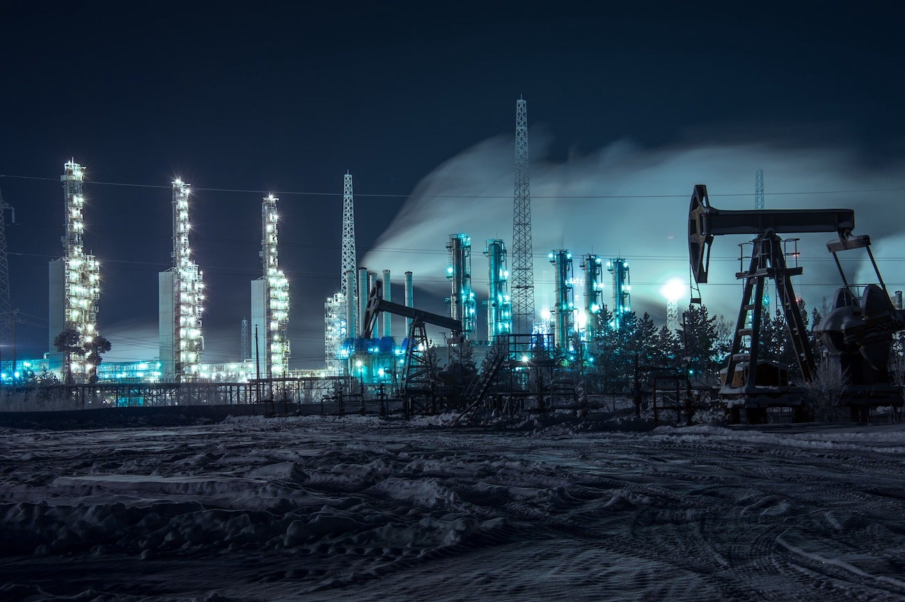 Oil rigs and brightly lit industrial site at night. Pump jack and grange mouth refinery at night. Toned.