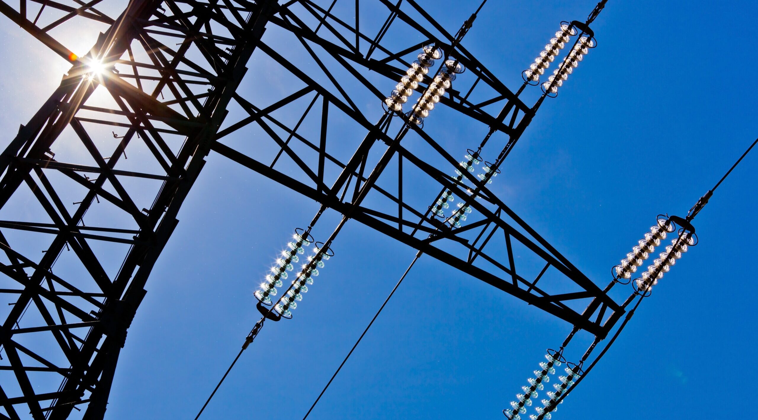 a high voltage pylon for electricity against a blue sky and sunbeams