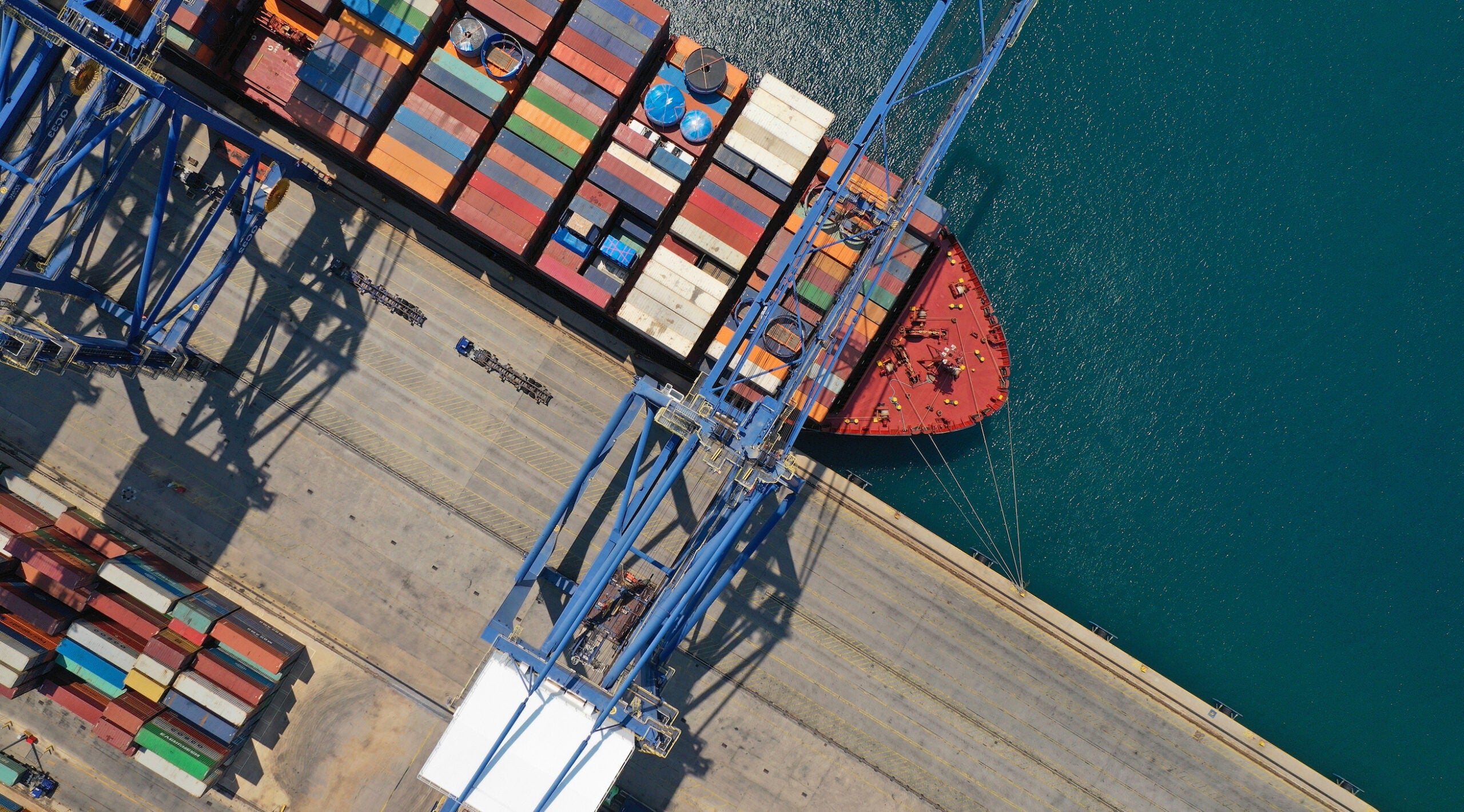 Maritime Terminal Operator Reduces Costs and Improves OT Security with Dragos. Aerial top down ultra wide photo of industrial cargo container ship loading in logistics terminal port.