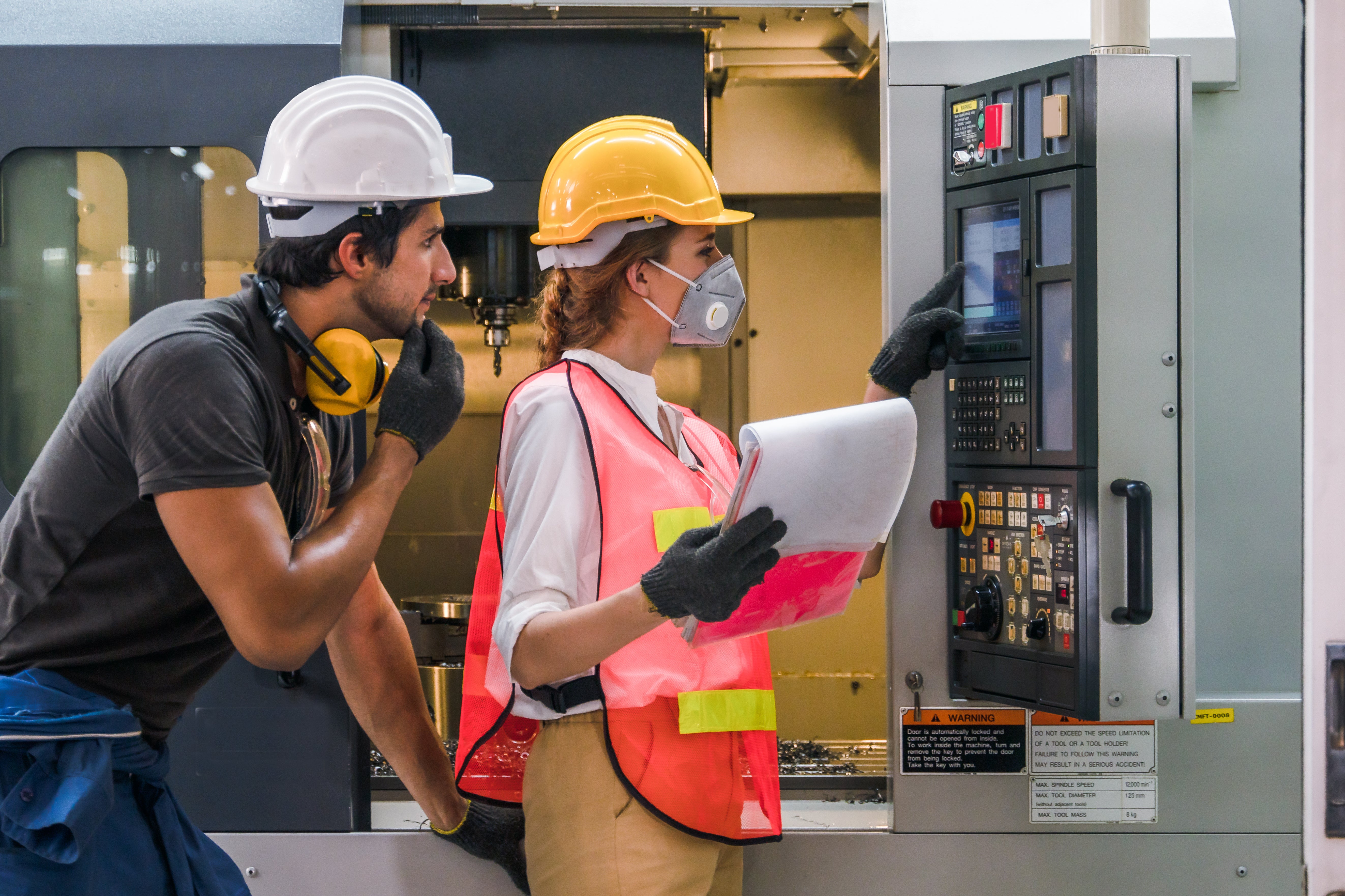 Two people in safety gear in front of an Engineer control panel