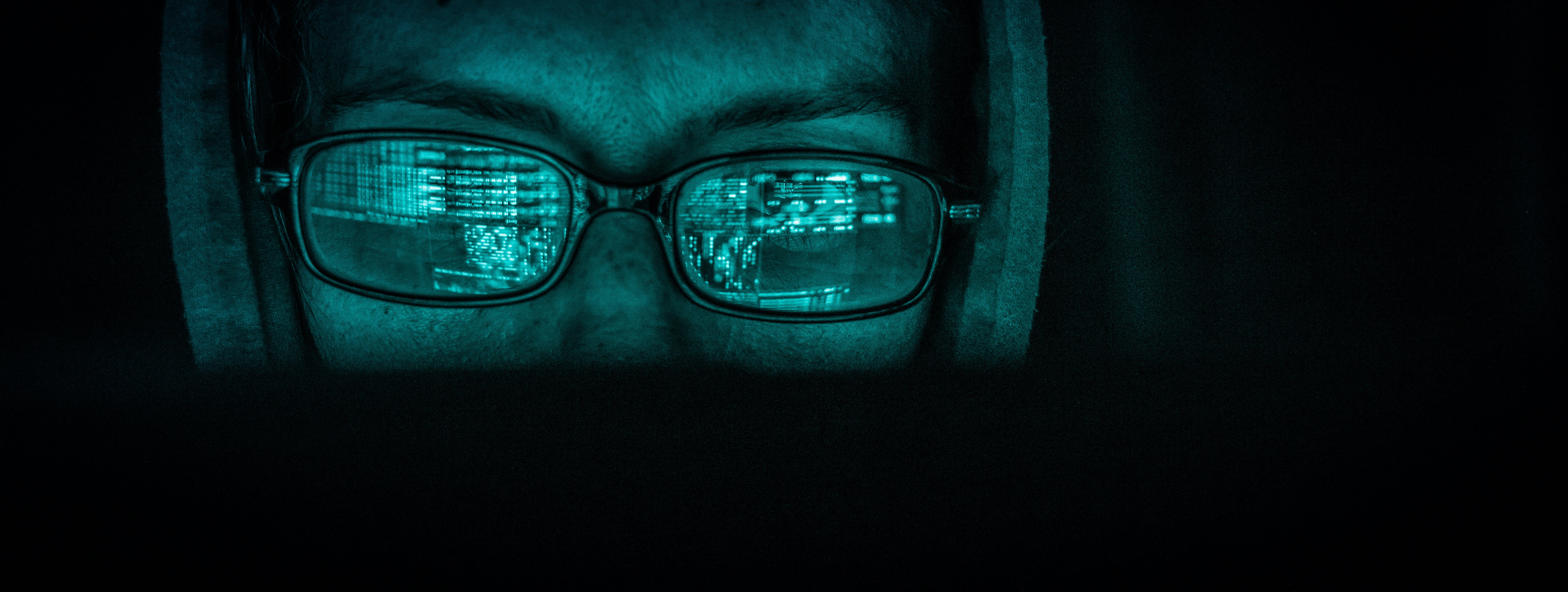 a photo of a person wearing rectangular glasses with a hoodie. The person has a glowing green filter over them to indicate they are adversarial